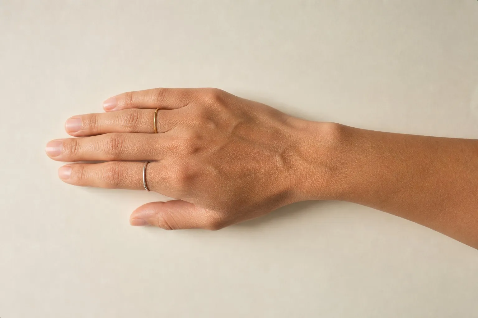 A hand resting on warm paper wearing a thin gold ring on the index finger and a thin silver ring on the ring finger