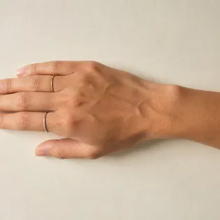 A hand on warm paper wearing a thin gold ring and a thin silver ring side by side