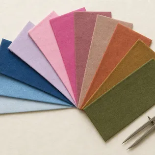 Twelve fabric swatches fanned out on warm paper, from icy blues and pinks through muted tones to rust and olive